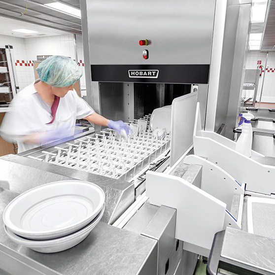 Staff member loading dishes into a HOBART industrial dishwasher in a professional kitchen