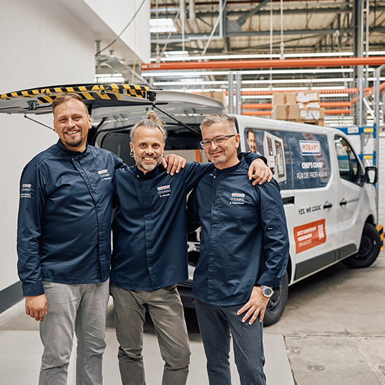 Three individuals in HOBART COOKING shirts standing in front of a branded van in an industrial setting