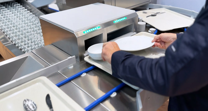 Close-up of the HOBART SMART LOAD loading system showing ergonomic placement of plates and bowls on a tray into designated openings for automated processing in a professional warewashing line.