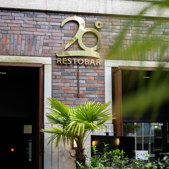 Exterior view of a brick building with the gold-colored sign 20° RESTOBAR above the entrance, partially framed by green plants.