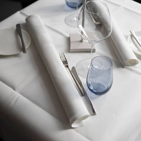 Elegantly set restaurant table with neatly arranged cutlery, wine glasses, rolled napkins and a textured blue water glass, creating a refined dining atmosphere.
