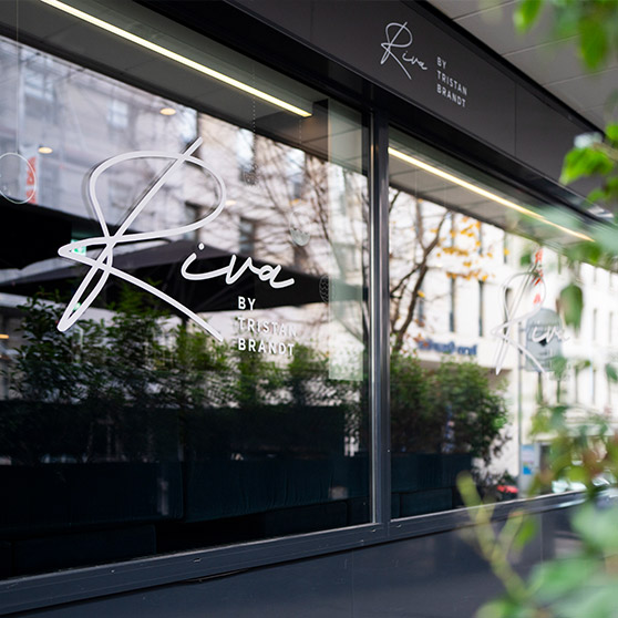 Exterior view of the RIVA by Tristan Brandt restaurant in Pforzheim featuring the signature logo on large glass windows facing the street.