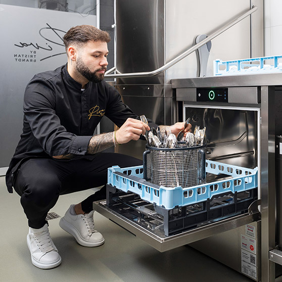 Staff member loading polished cutlery into the rotating BESTECK PREMIUM basket of a HOBART undercounter dishwasher designed for efficient and spotless cutlery cleaning.