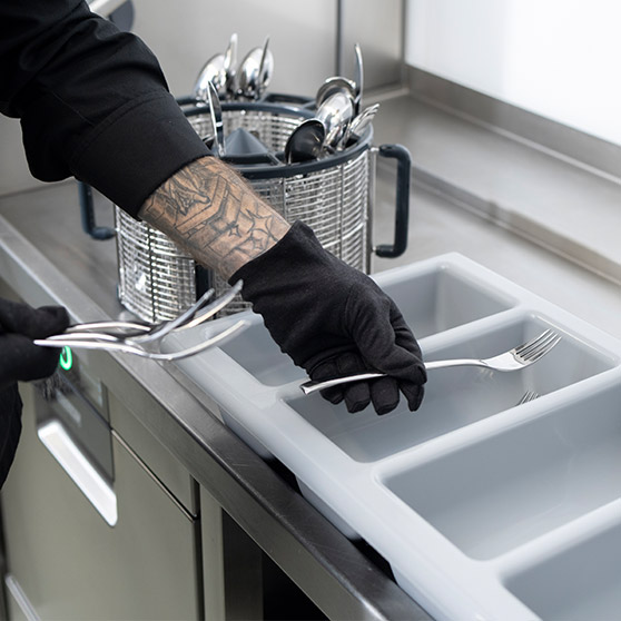 Close‑up of a staff member sorting freshly washed cutlery next to a HOBART undercounter dishwasher equipped with the BESTECK PREMIUM feature.