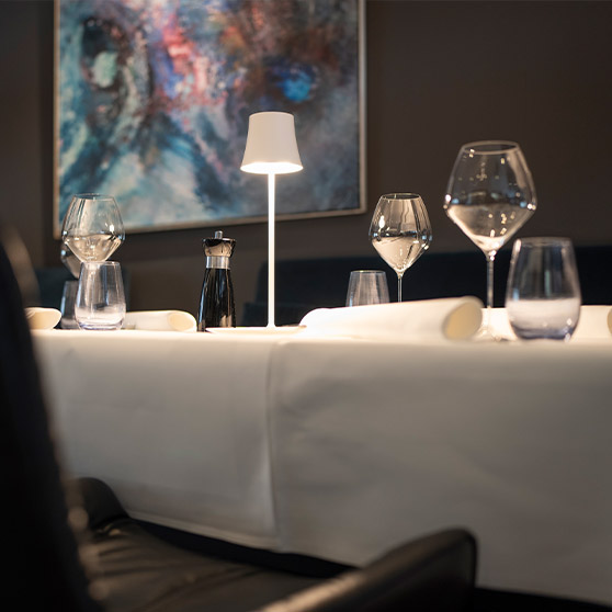 Close‑up of a fine‑dining table setting with elegant glassware, white linens, modern lighting and refined table accessories in the RIVA restaurant.