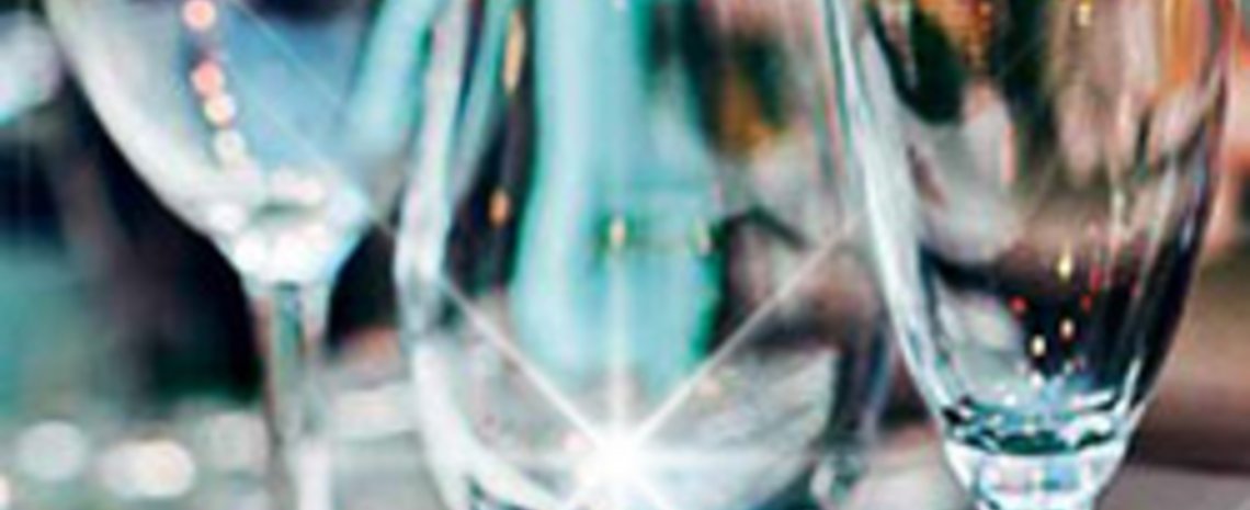 A close-up view of several polished drinking glasses standing upright, reflecting bright light points and colorful background reflections.