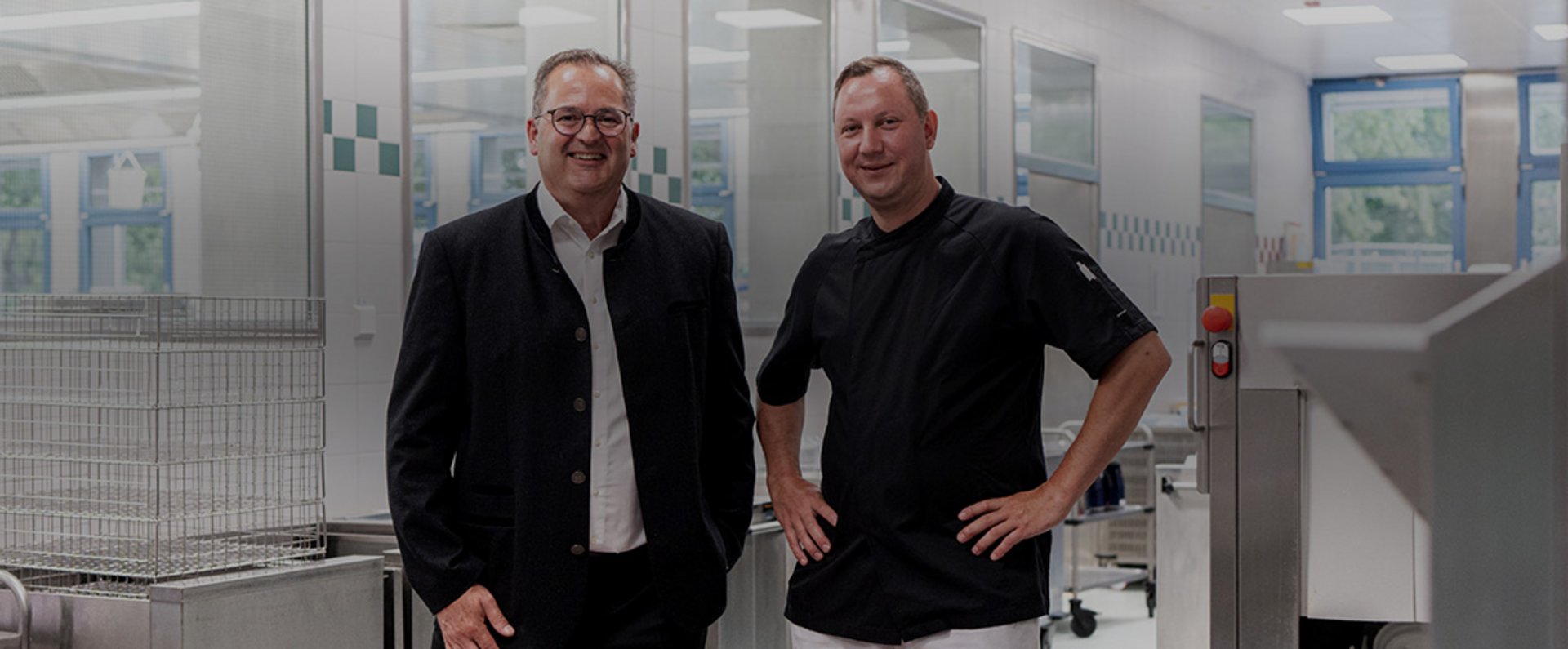 Two individuals stand in the dishwashing area of the Garmisch‑Partenkirchen hospital kitchen in front of the HOBART autoLINE system, highlighting the modernized installation within the hygienic workspace.