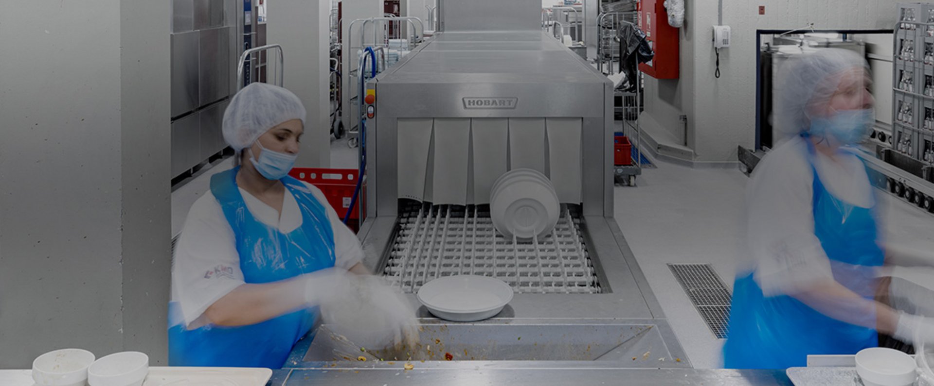 In the dishwashing area of the University Hospital Mannheim, trays, bowls, and plates are placed onto the automated intake of a HOBART FTNi conveyor dishwashing system, demonstrating an efficient, hygiene‑safe setup designed for the continuous cleaning demands of large‑scale hospital meal service.