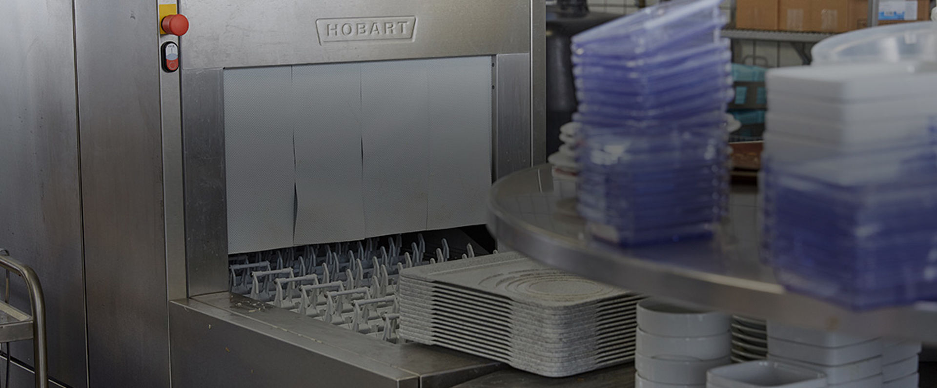 HOBART conveyor dishwasher with stacks of trays and containers positioned for high‑volume cleaning as part of a streamlined dishwashing workflow in a commercial kitchen.