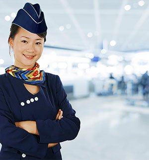 Person in a dark blue uniform with matching hat and colorful neck scarf standing in an airport terminal.