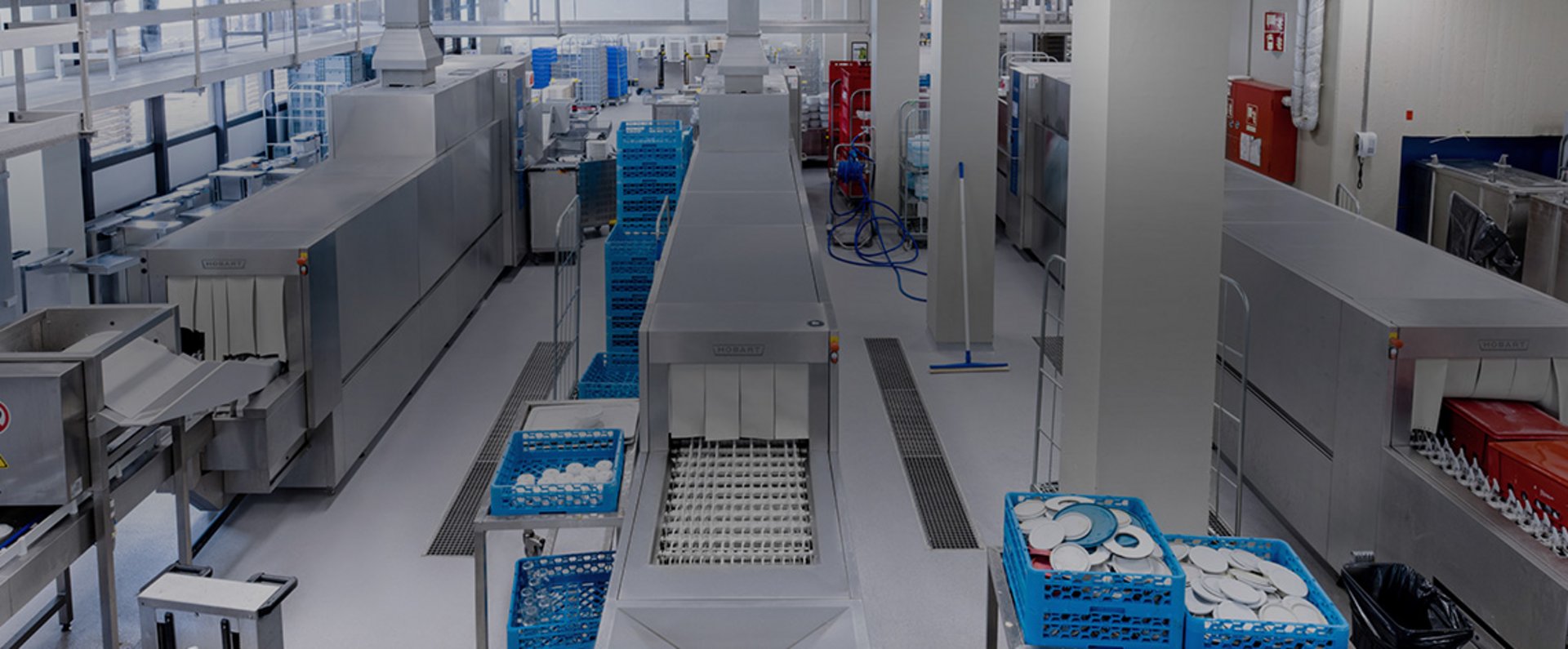 The dishwashing area of the University Hospital Mannheim features multiple HOBART FTNi conveyor dishwashers operating alongside an extensive automated transport system, ensuring efficient, hygiene‑safe cleaning of large quantities of trays, racks, and dishware required for continuous high‑volume hospital meal service.