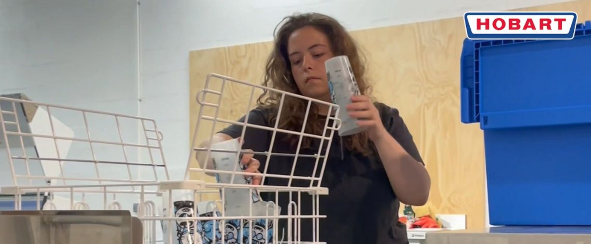 Worker organizing reusable event cups into a dedicated washing rack at the OECO central cleaning facility in Paris, preparing them for processing in the HOBART PROFI CN conveyor dishwasher.