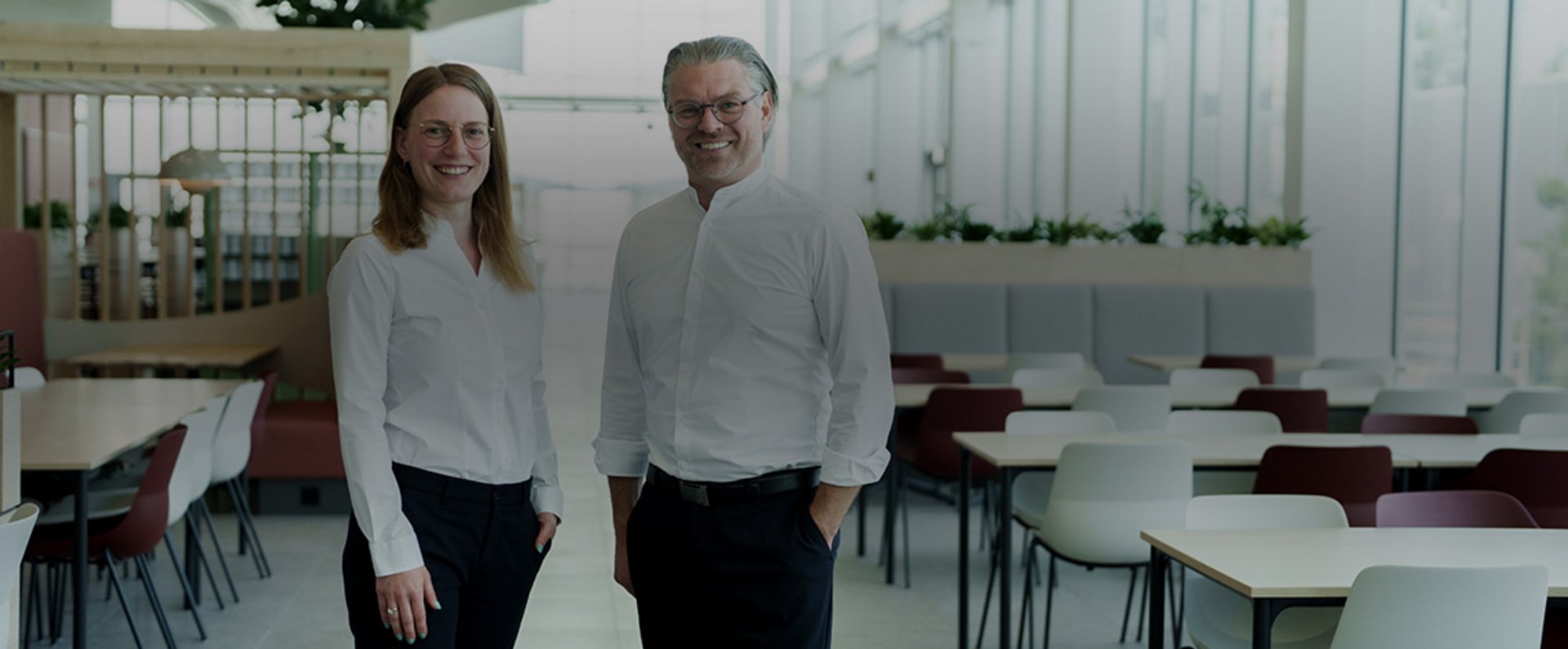 Two employees standing inside the modern MTU Aero Engines company restaurant, surrounded by contemporary seating areas and bright architectural design.