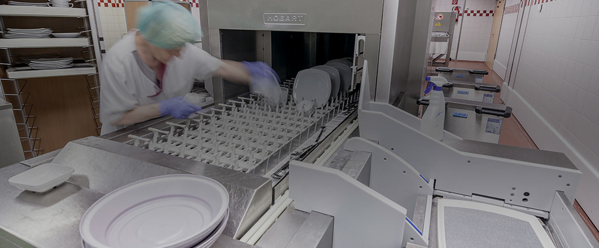 Staff member placing plates into the intake section of the HOBART AutoLINE in the SHG Clinic Völklingen, where the integrated system washes trays, cutlery, and dishware simultaneously.