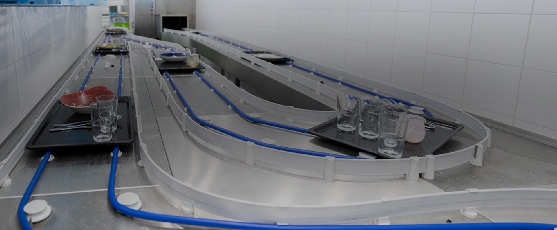 Automated tray return system at the MTU facility showing trays with dishes moving along guided conveyor tracks toward the dishwashing area.