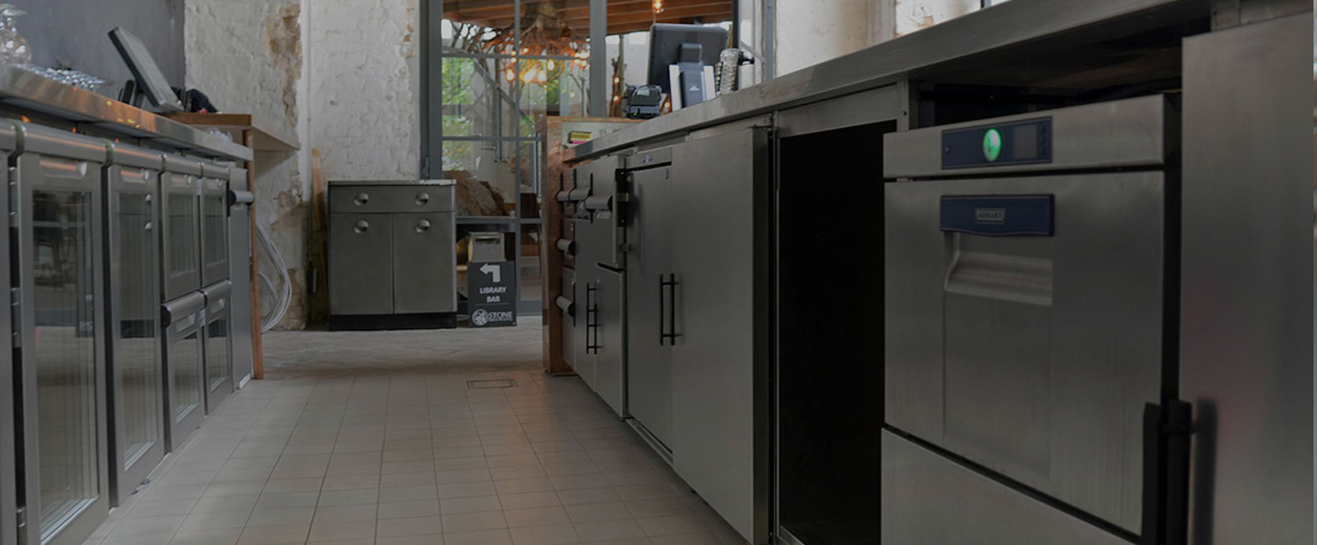 Undercounter dishwashing stations equipped with HOBART technology in the Stone Brewing Berlin bar area, integrated into a stainless steel workspace for seamless service operations.