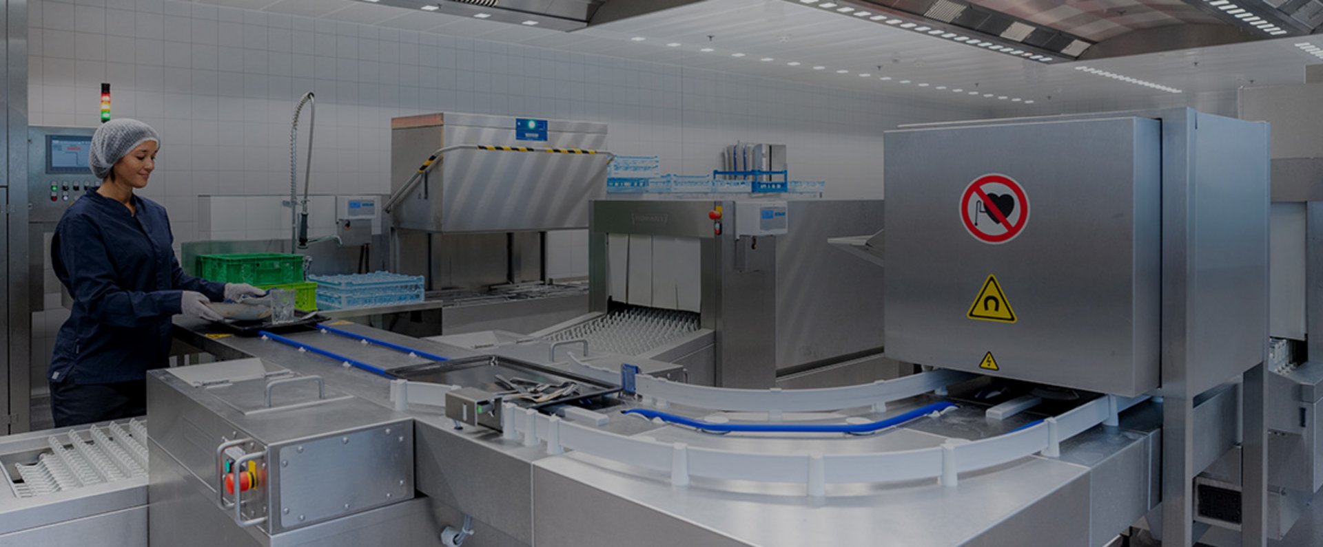 Staff member operating a workstation with integrated conveyor technology and HOBART dishwashing machinery designed to handle large quantities of trays and dishware efficiently at the MTU facility.