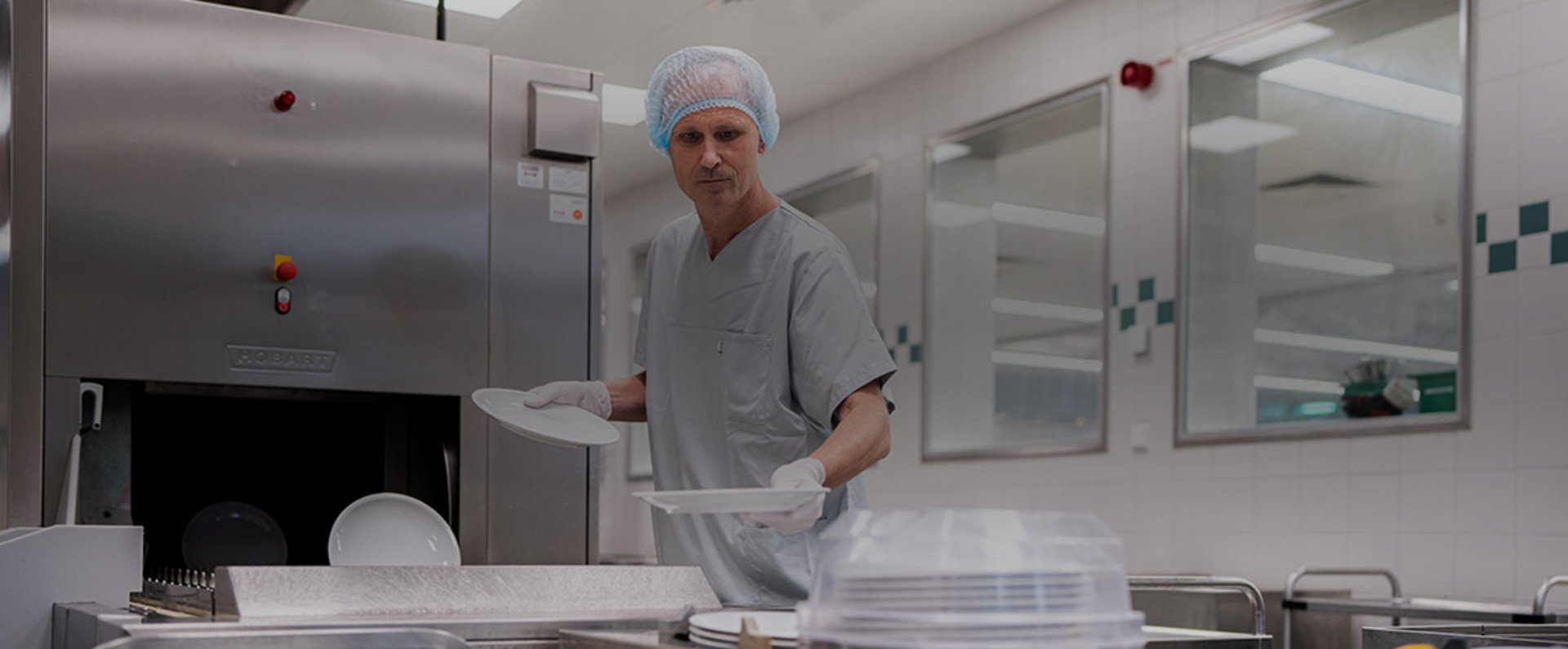A person places plates into the intake area of the HOBART autoLINE conveyor dishwashing machine in the Garmisch‑Partenkirchen hospital kitchen, supporting an efficient high‑volume cleaning process.